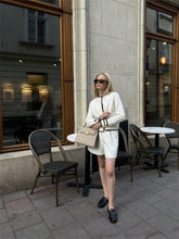 A woman wearing a white cardigan and carrying a gray handbag.
